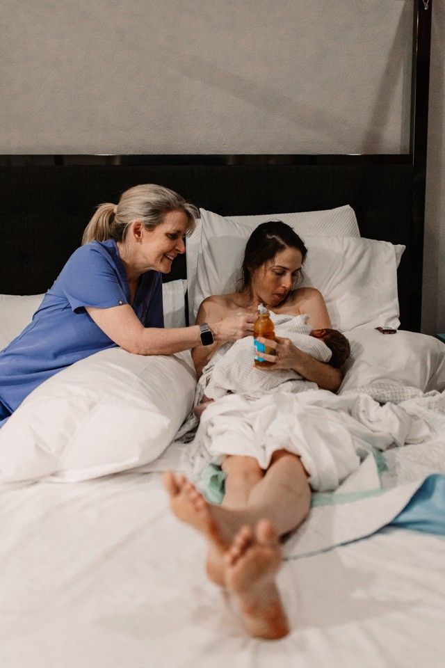 A nurse is feeding a newborn baby on a bed.