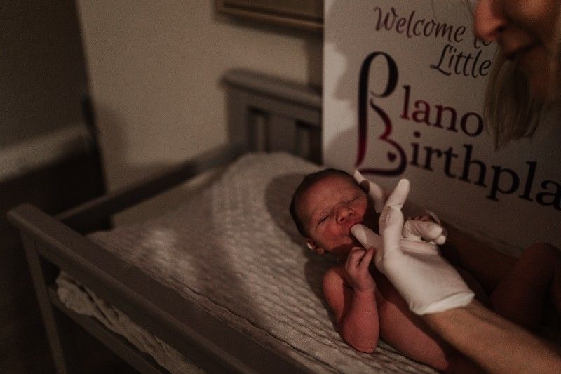 A newborn baby is being held by a man in front of a welcome little piano birthplace sign.