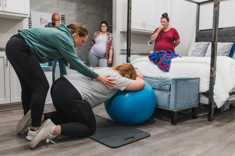 A woman is helping a pregnant woman with a birthing ball.