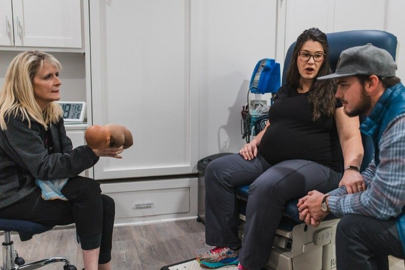 A pregnant woman is sitting in a chair talking to a man and a woman.
