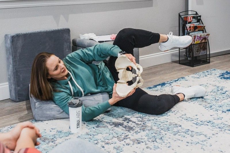 A woman is laying on the floor holding a skeleton.