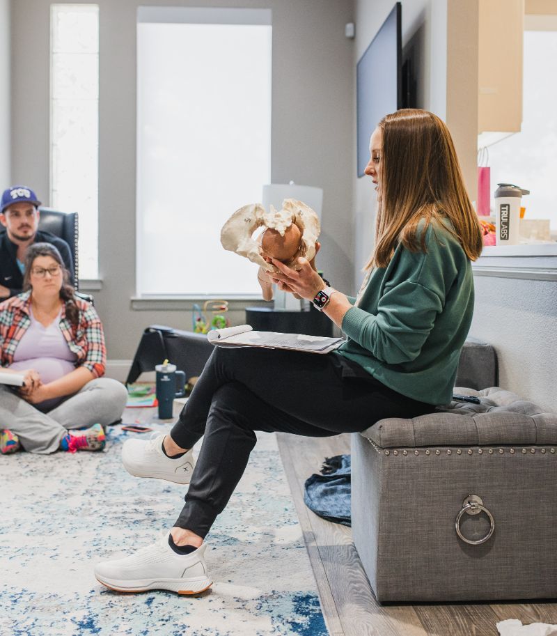 A woman is sitting on an ottoman holding a skeleton of a baby