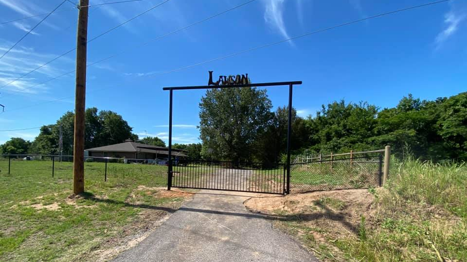 A gate leading to a house in the middle of a field.