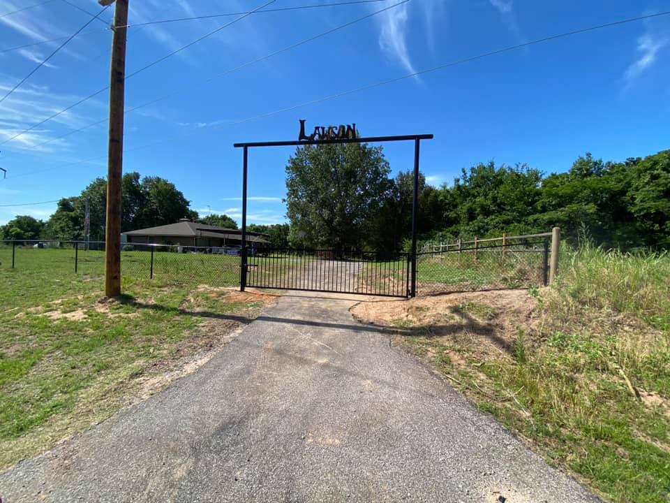 A road with a gate on the side of it leading to a house.