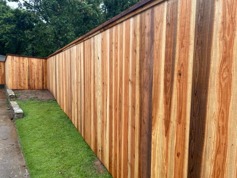 A long wooden fence surrounds a lush green yard.