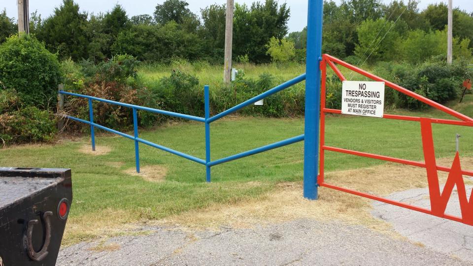 A red and blue fence with a horseshoe on it is surrounded by grass and trees.