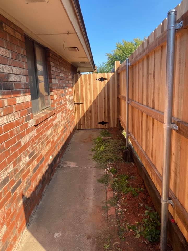 A wooden fence is between a brick building and a sidewalk.