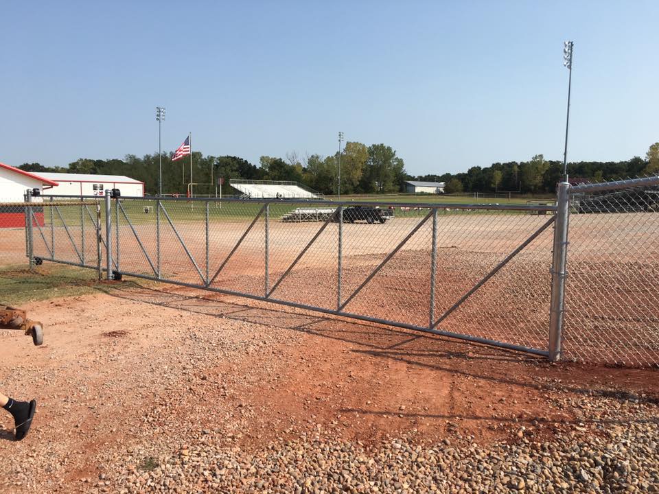 A chain link fence is surrounding a dirt field.