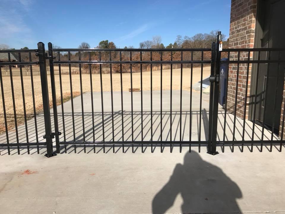 A shadow of a person is cast on the sidewalk in front of a fence.