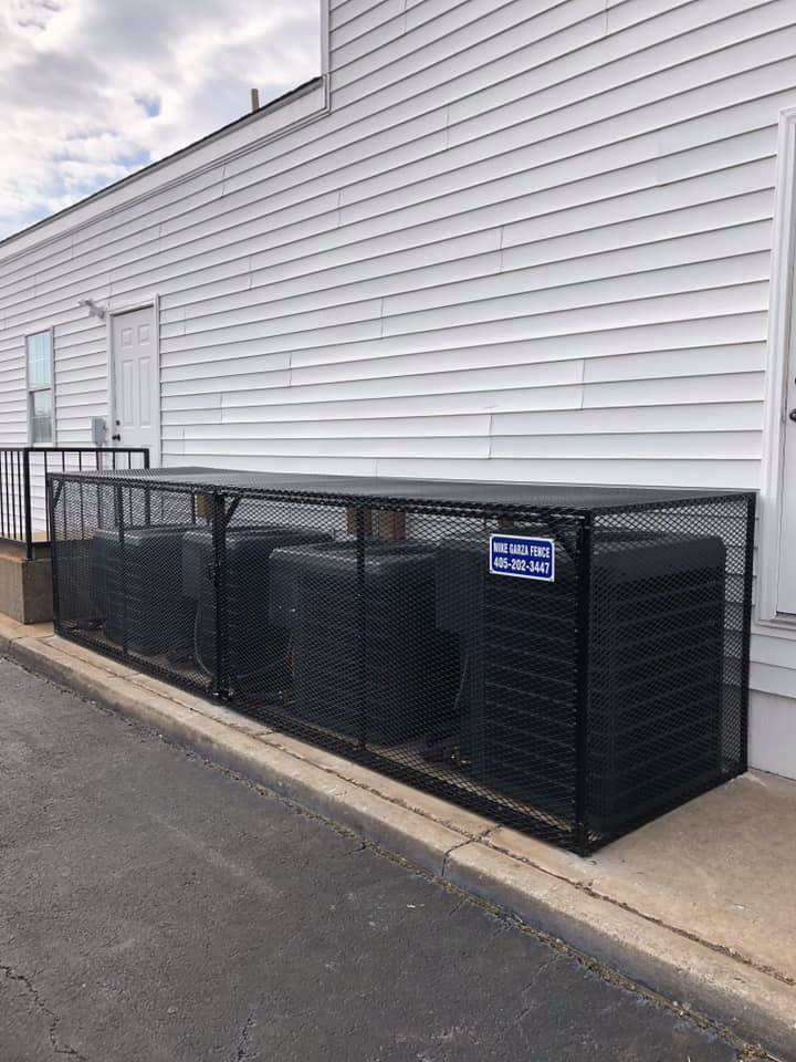 A row of air conditioners are sitting inside of a metal cage on the side of a building.