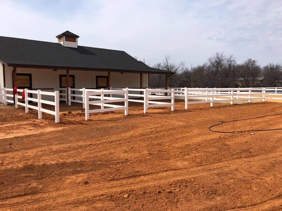 A white fence surrounds a dirt field in front of a house