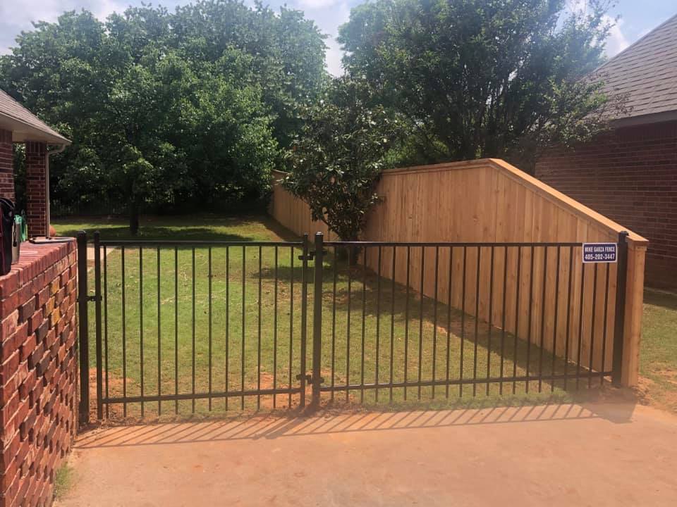 A metal gate is surrounded by a wooden fence and a brick wall.