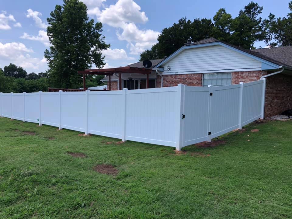 A white fence surrounds a lush green yard in front of a house.