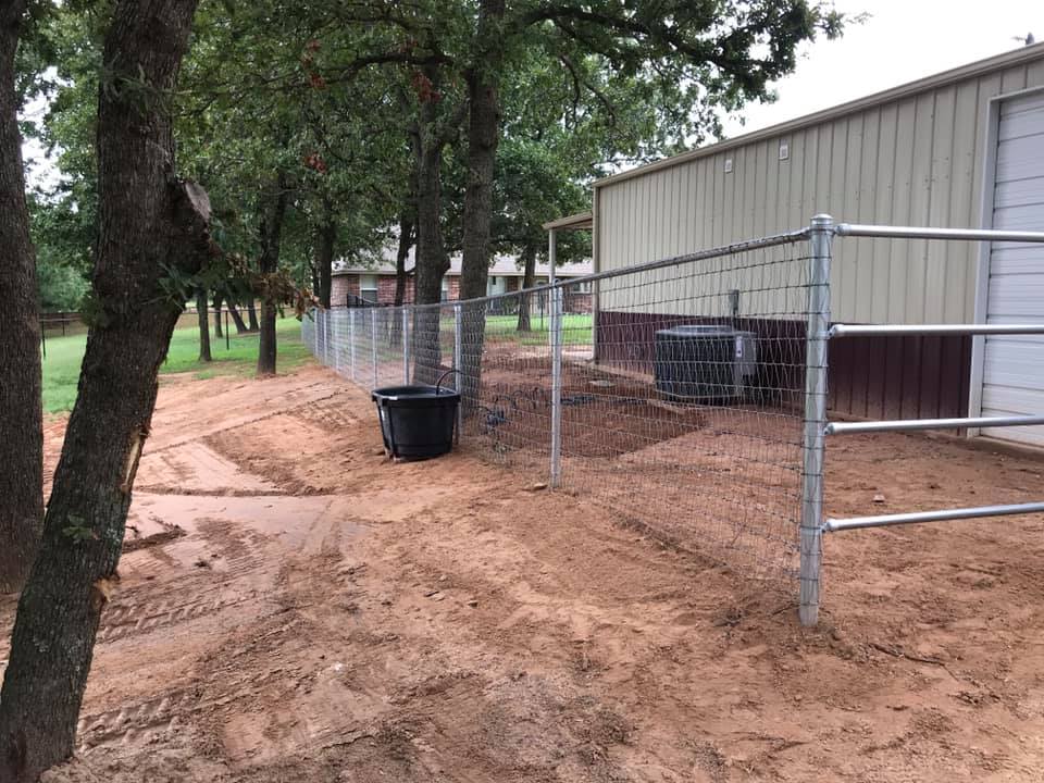 A metal fence is surrounding a dirt area in front of a building.