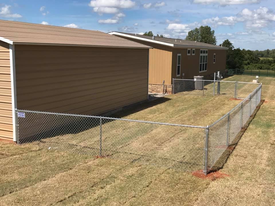 A chain link fence is surrounding a mobile home in a field.