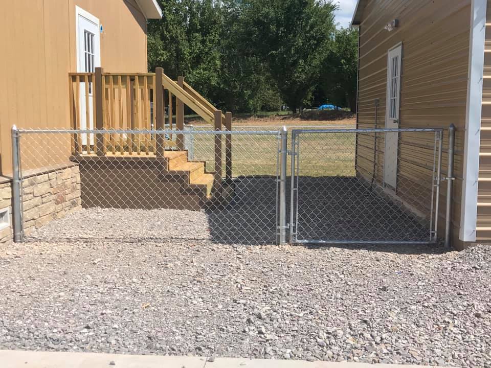 A chain link fence surrounds a gravel yard in front of a house.