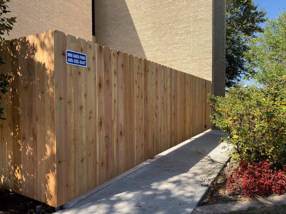 A wooden fence is surrounding a concrete walkway next to a building.