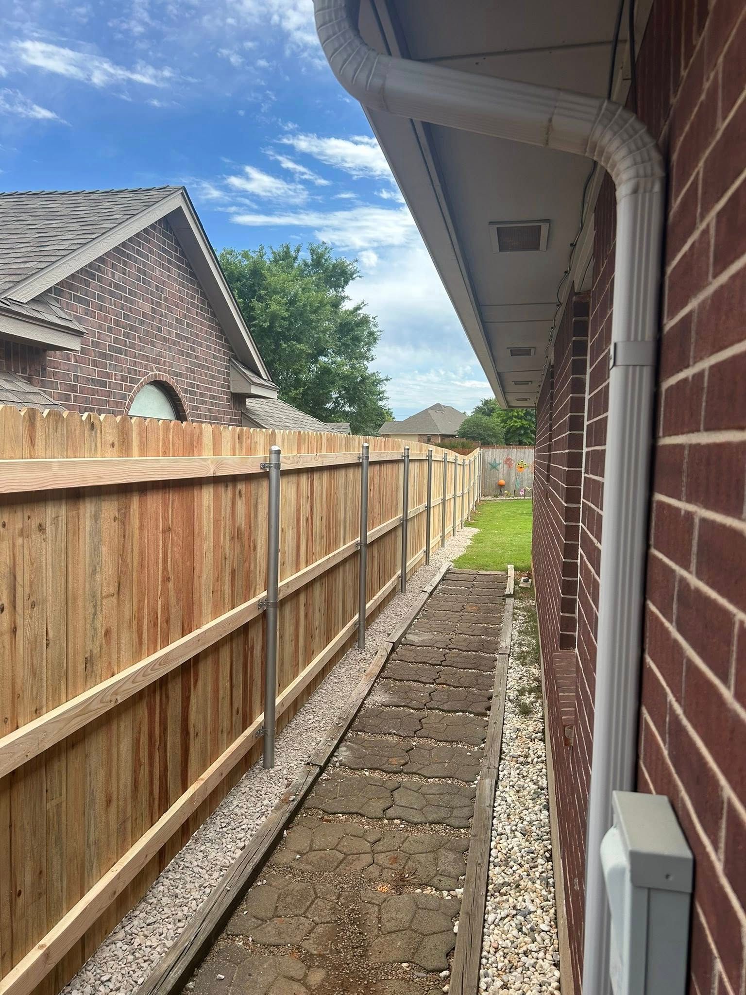 A wooden fence is along the side of a brick house.