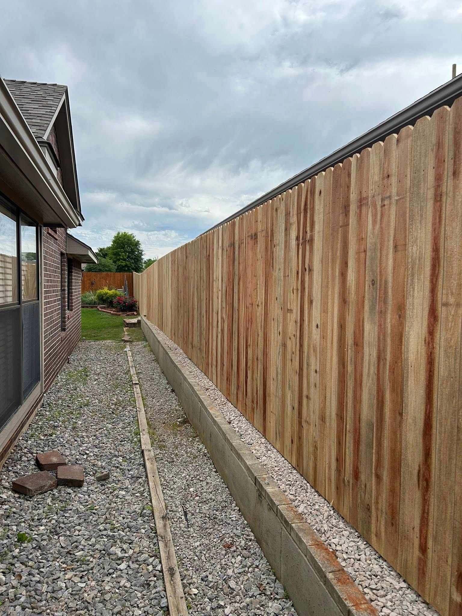 A wooden fence surrounds a gravel path in front of a house.