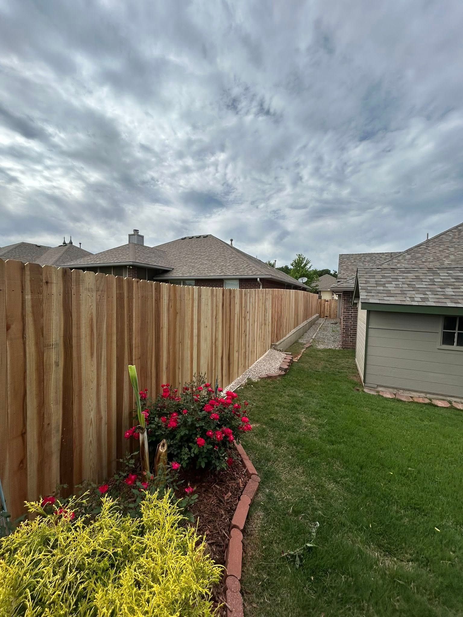 A wooden fence surrounds a lush green yard with a house in the background.