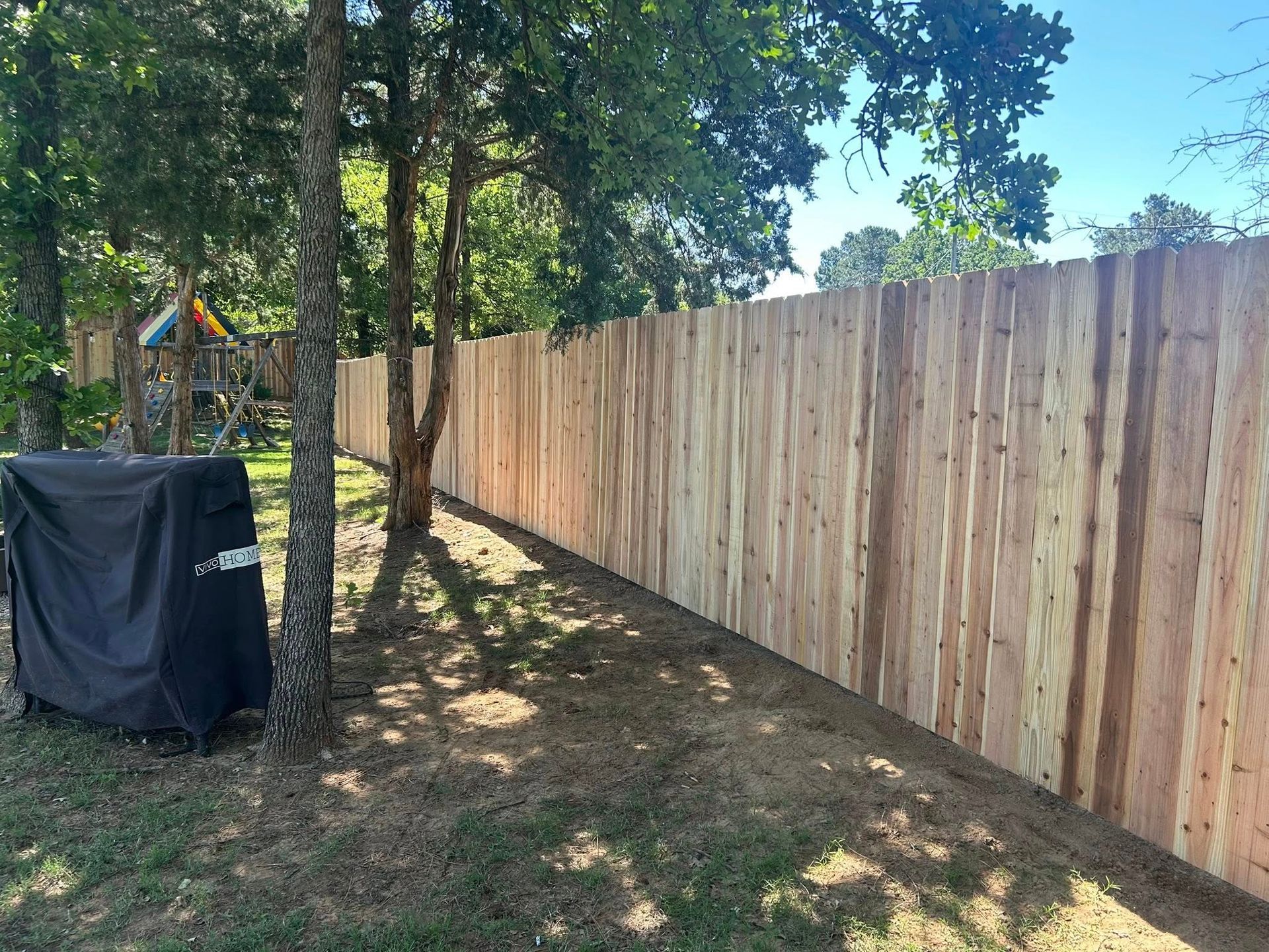 A wooden fence is surrounded by trees in a backyard.