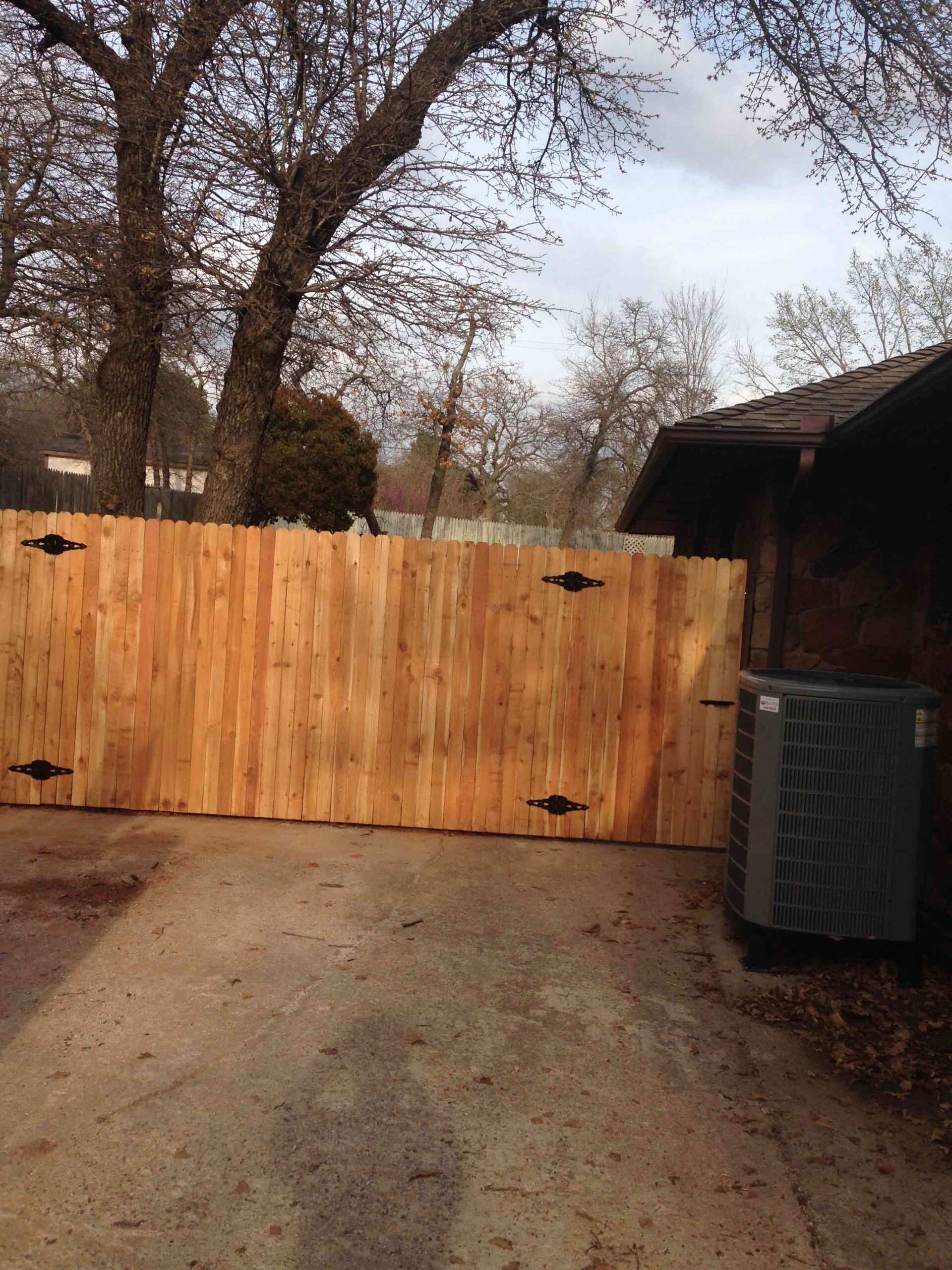 A wooden fence is surrounding a house with trees in the background