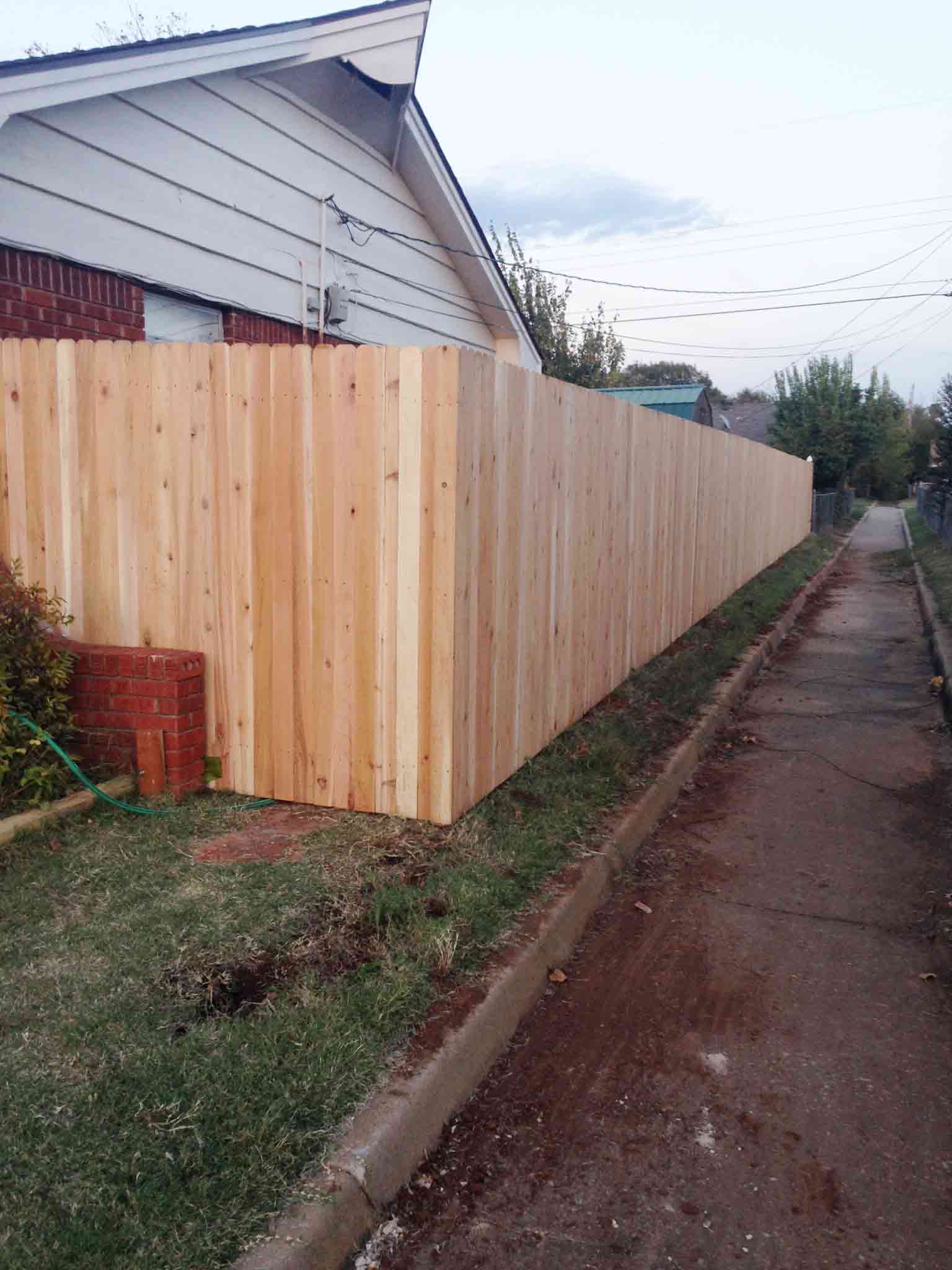 A wooden fence is sitting next to a sidewalk in front of a house.