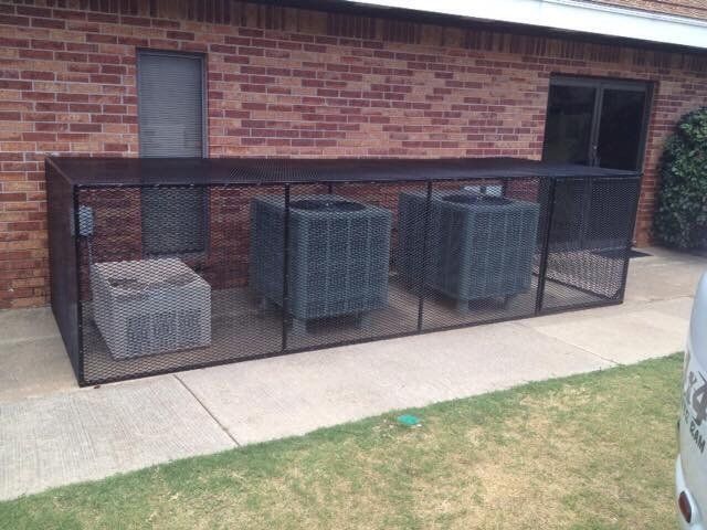 Three air conditioners are sitting under a fence in front of a brick building.