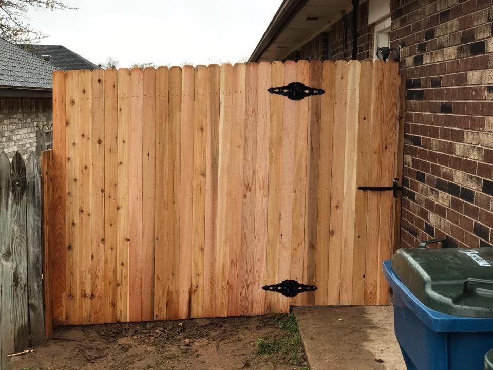 A wooden fence with a blue trash can in front of it