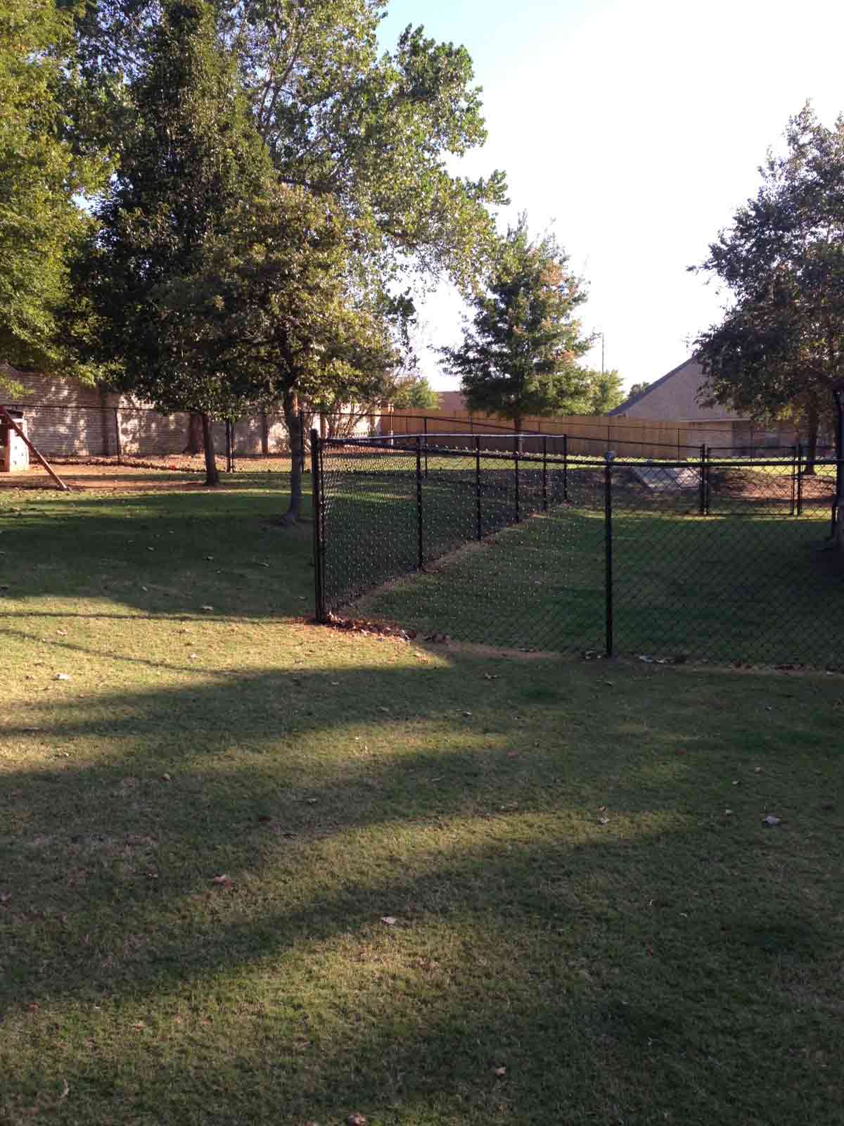 There is a chain link fence in the middle of a lush green field.