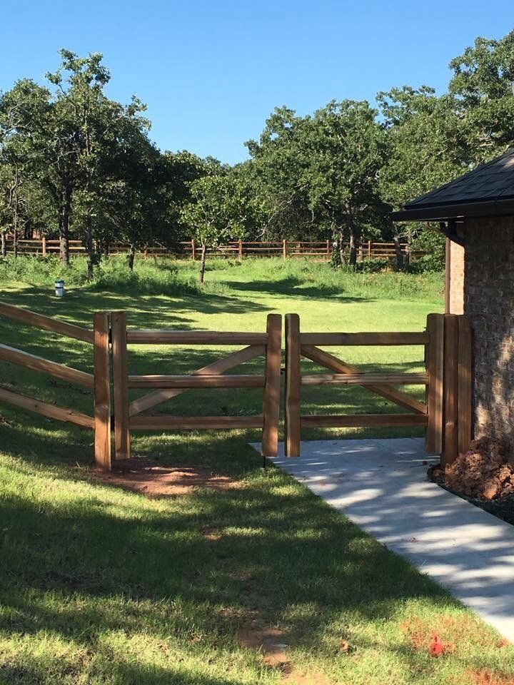 A wooden fence surrounds a grassy field with trees in the background
