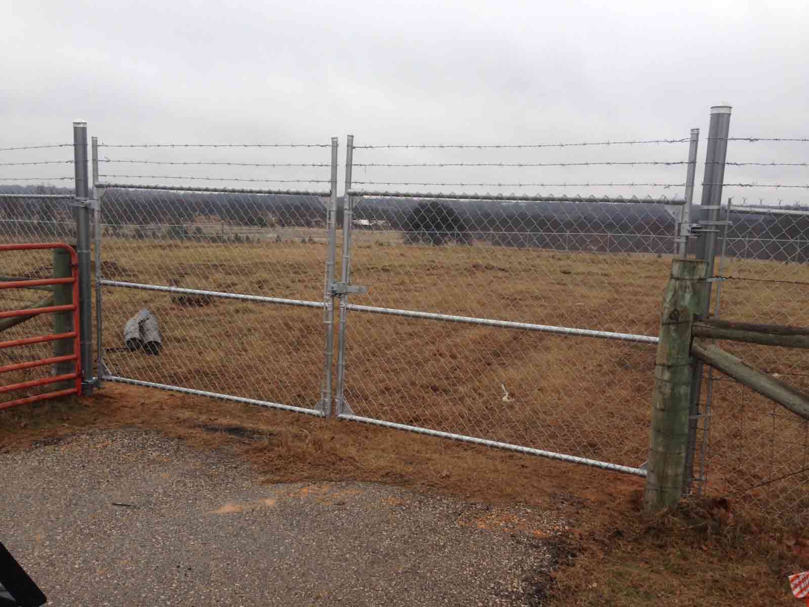 A chain link fence with barbed wire surrounding a field.