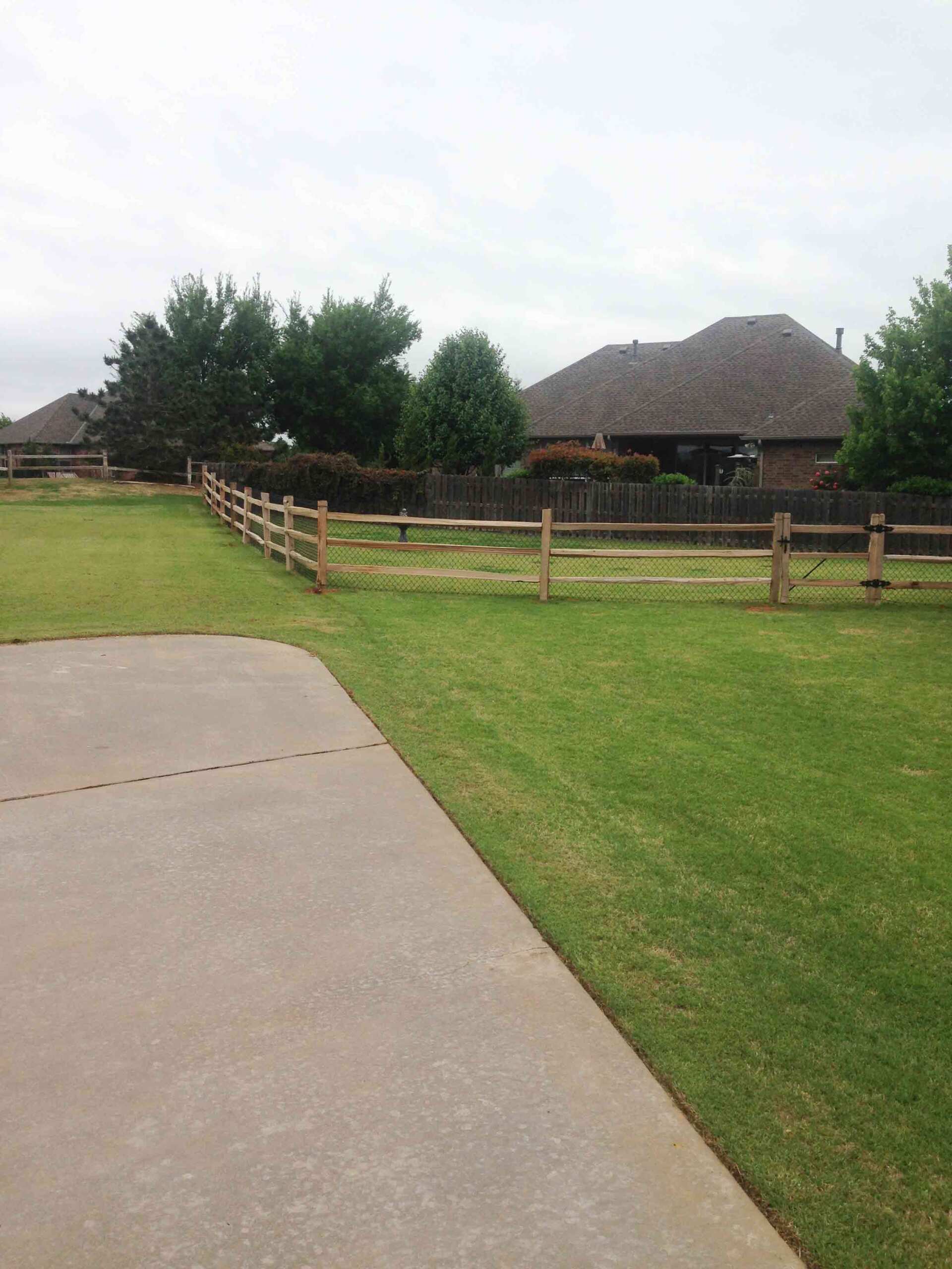 A driveway with a wooden fence and a house in the background.