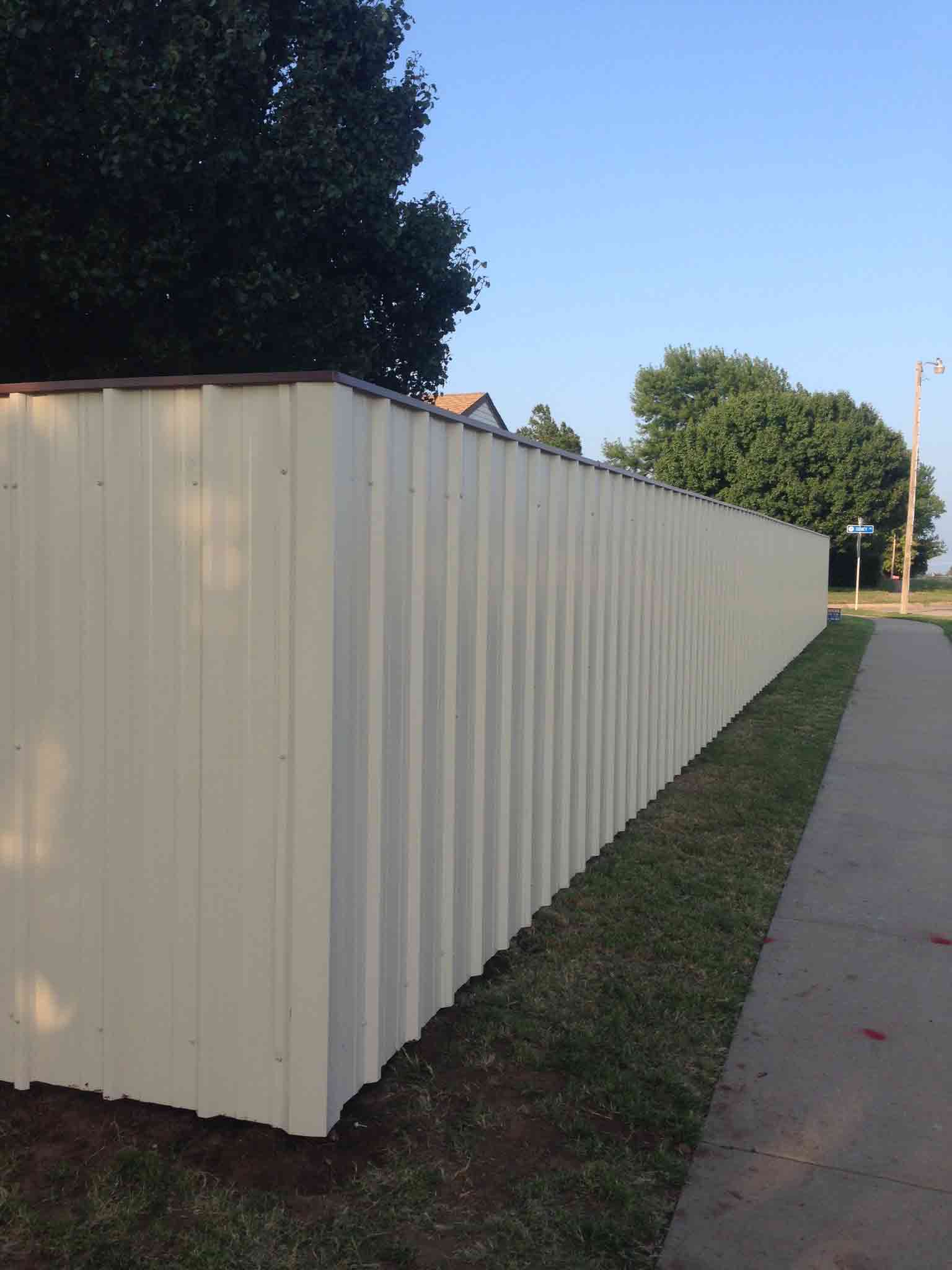 A white metal fence is sitting next to a sidewalk.