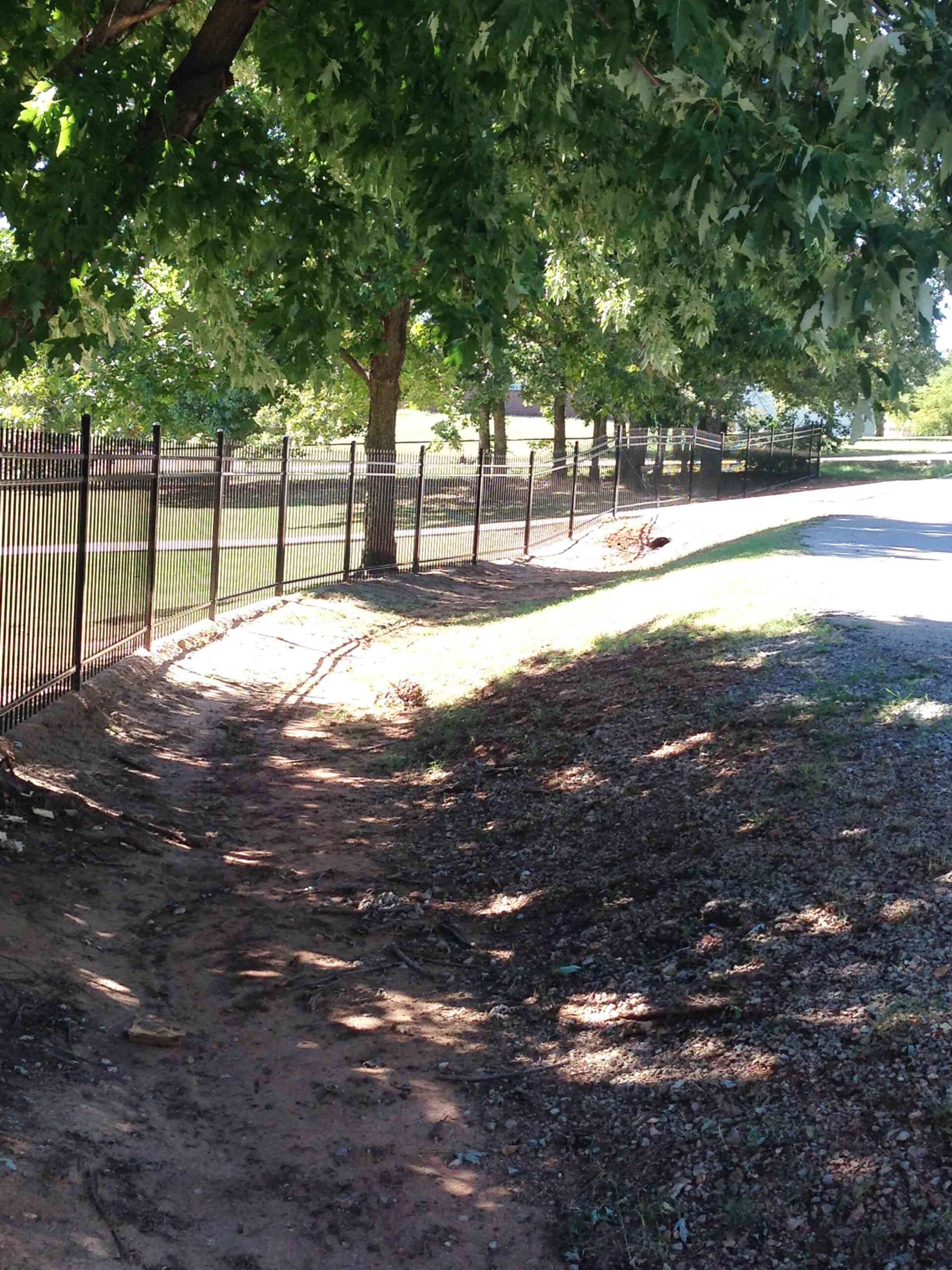 A dirt road with a fence and trees on the side of it.