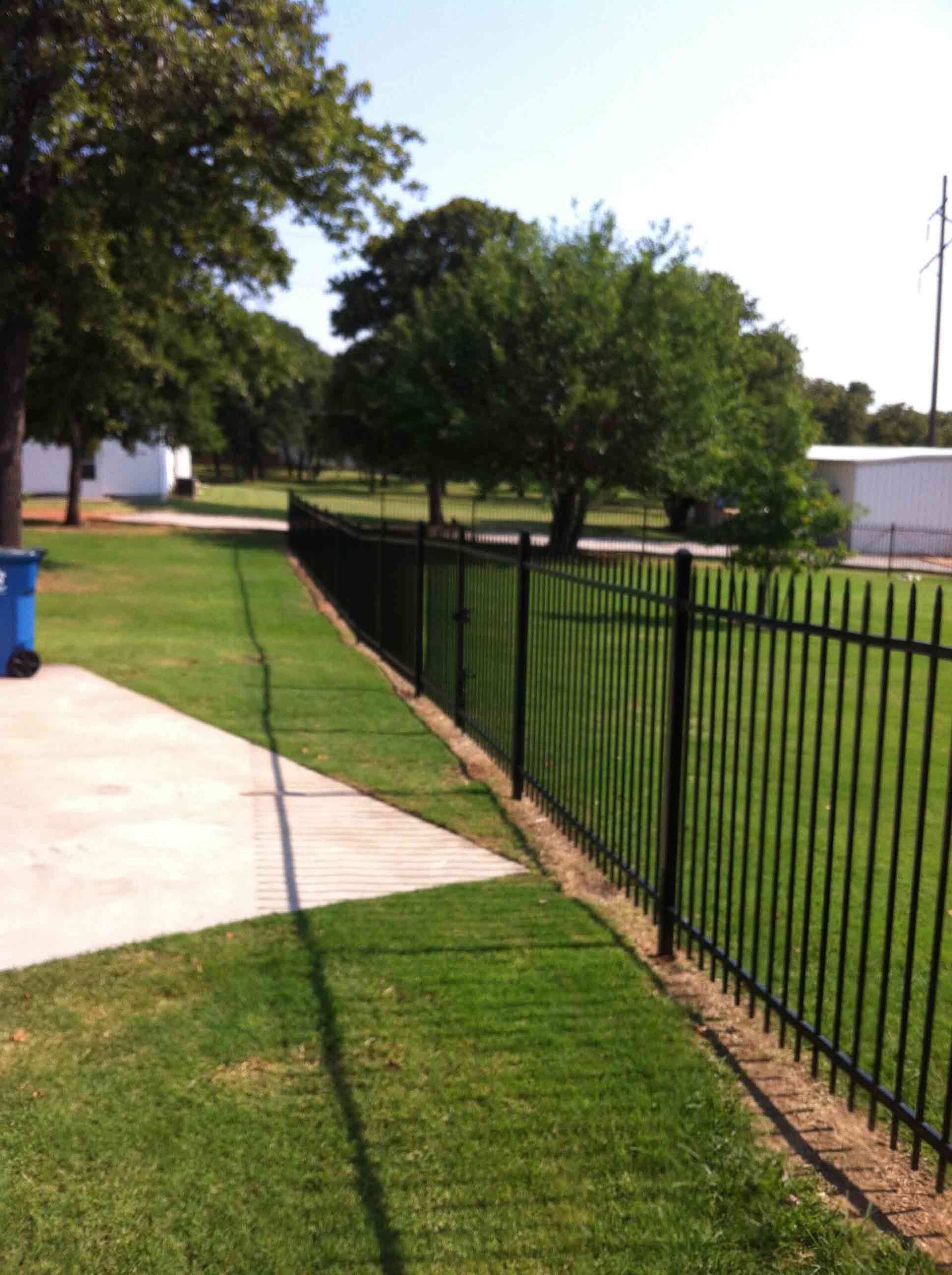 A black metal fence surrounds a lush green field