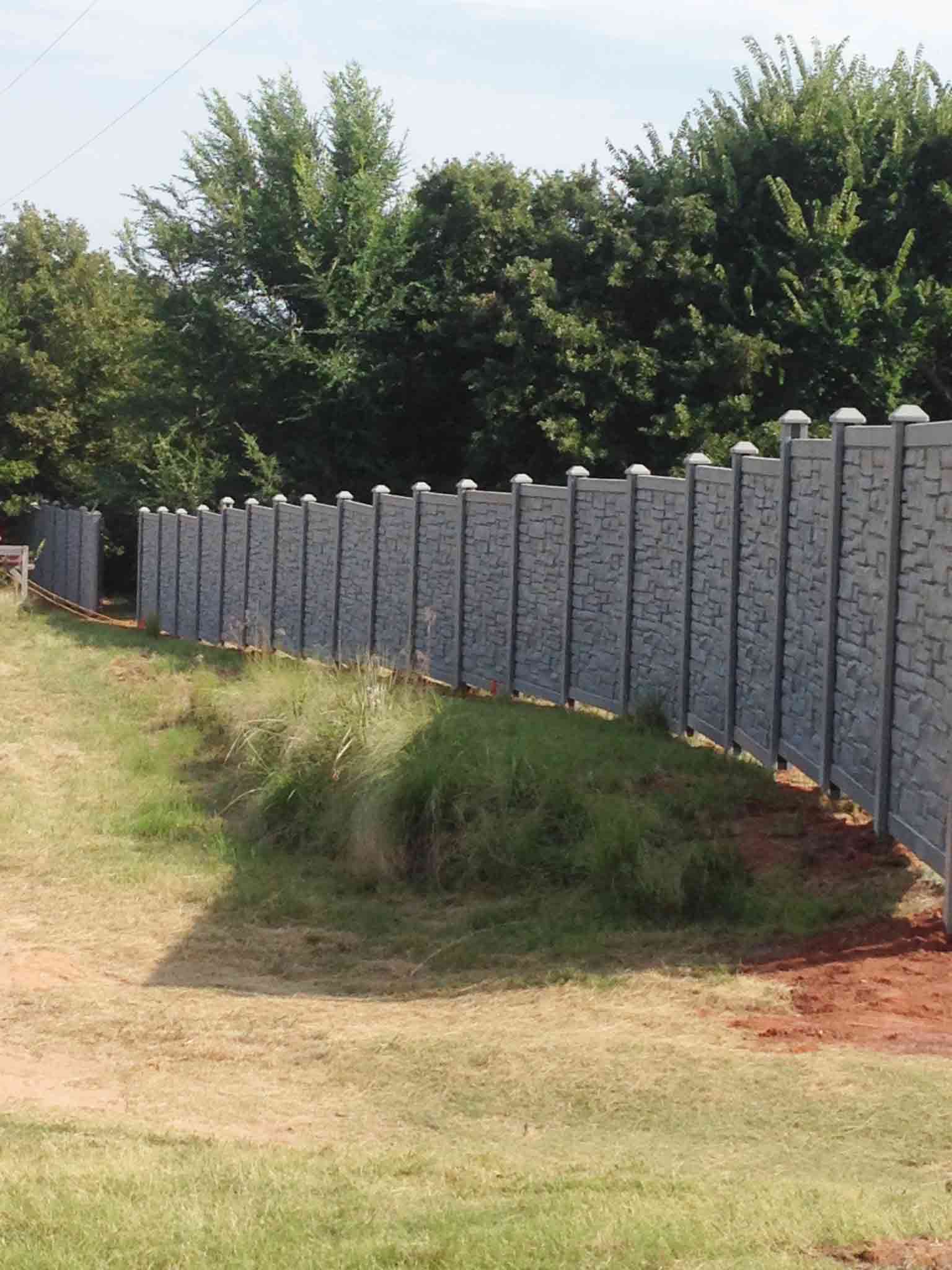 A concrete fence surrounds a grassy field with trees in the background.