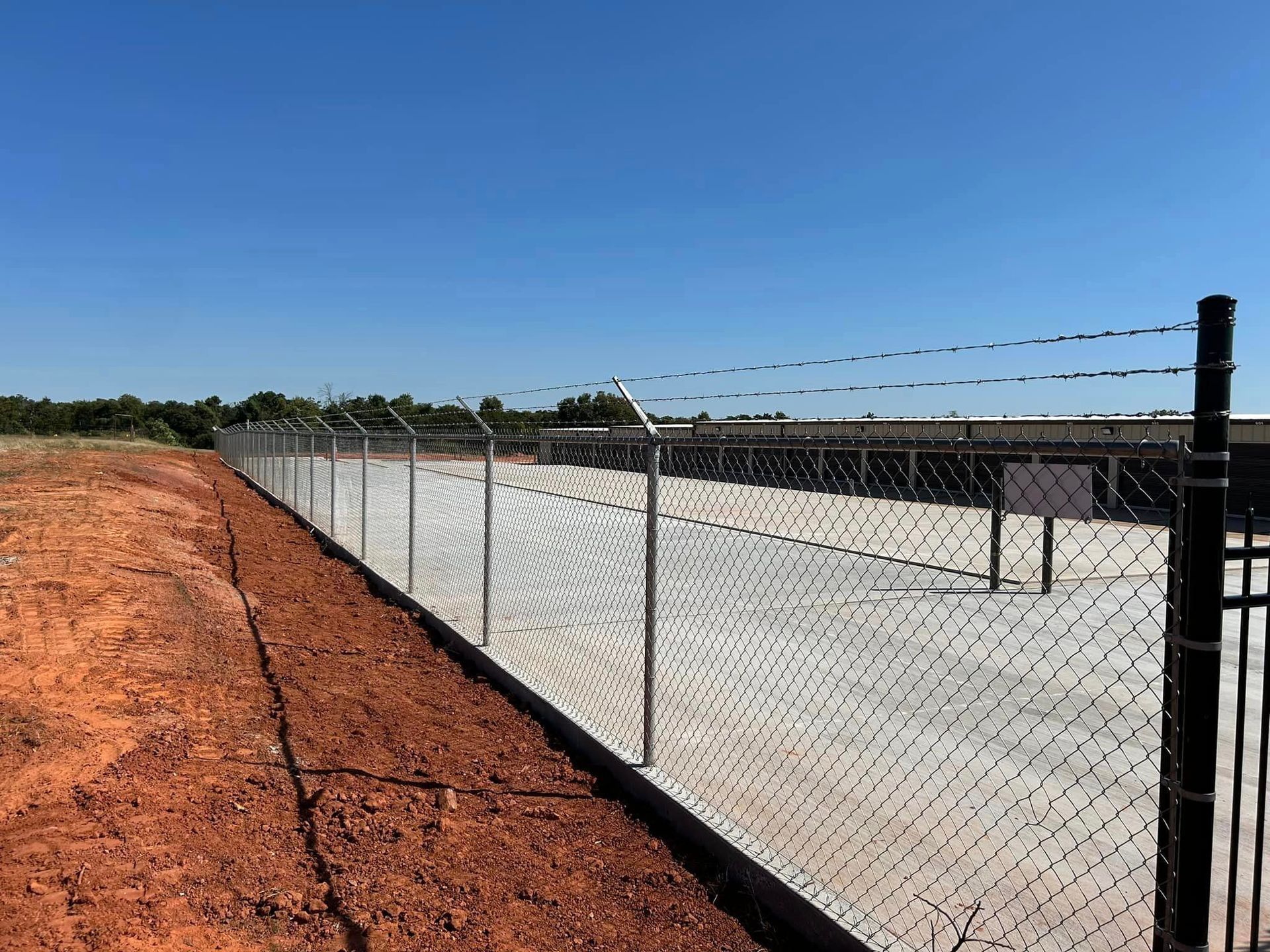 A chain link fence is surrounding a dirt field.