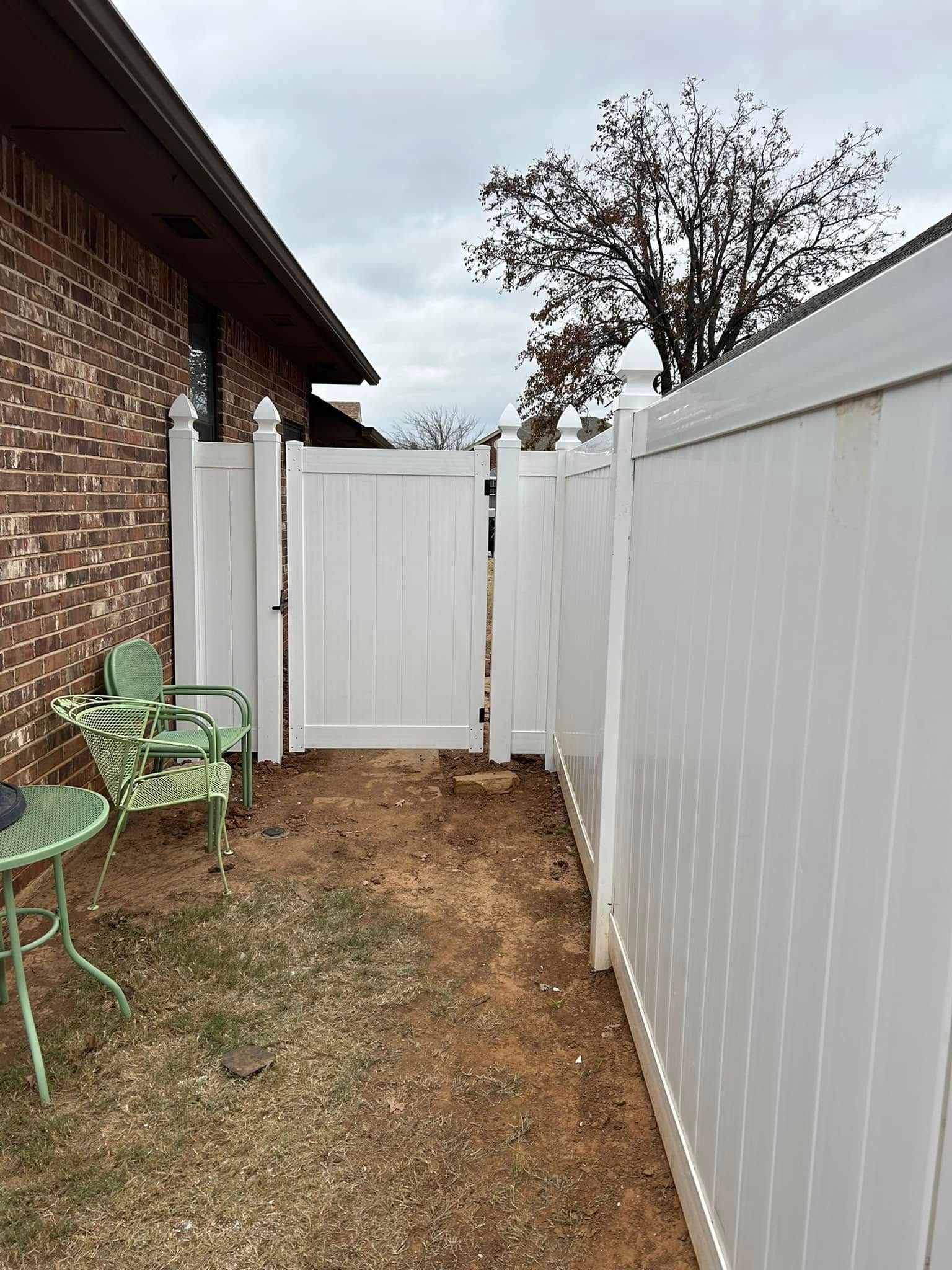 A white fence with a gate in the backyard of a house.