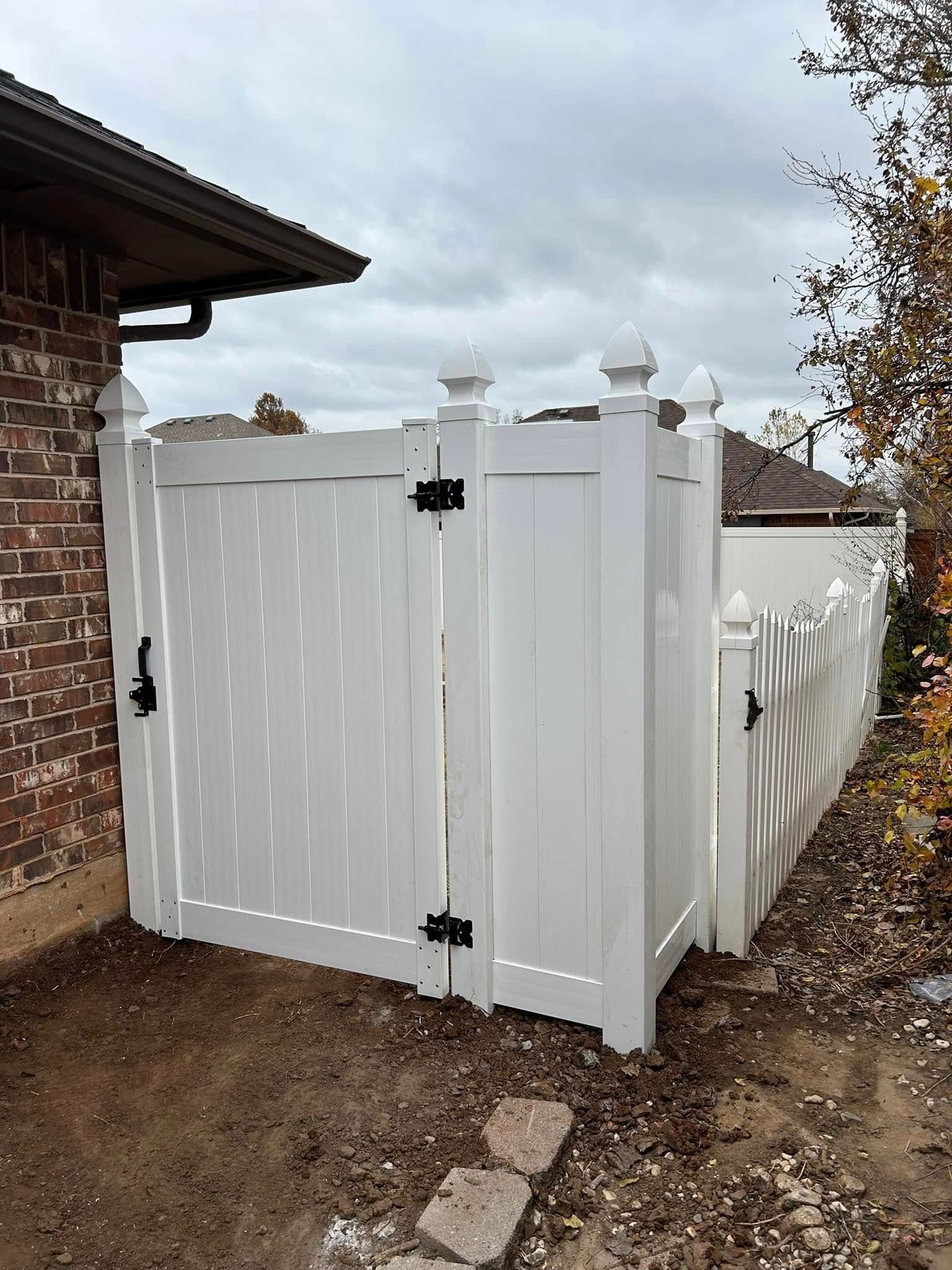 A white fence with a gate in front of a brick house.