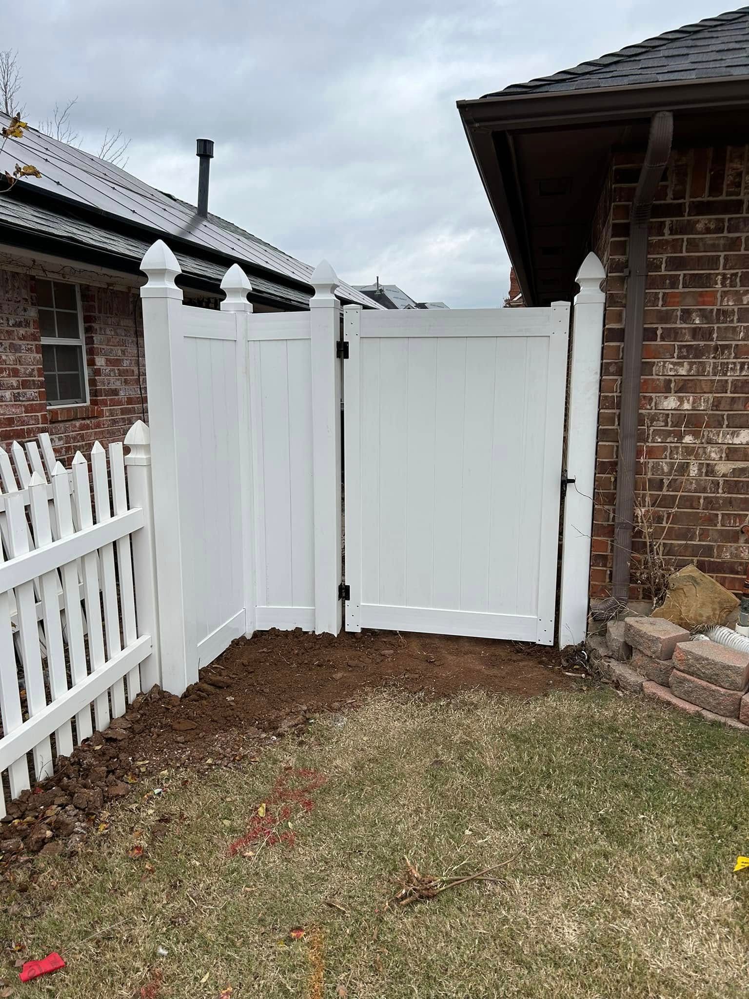 A white fence with a gate in front of a brick house.