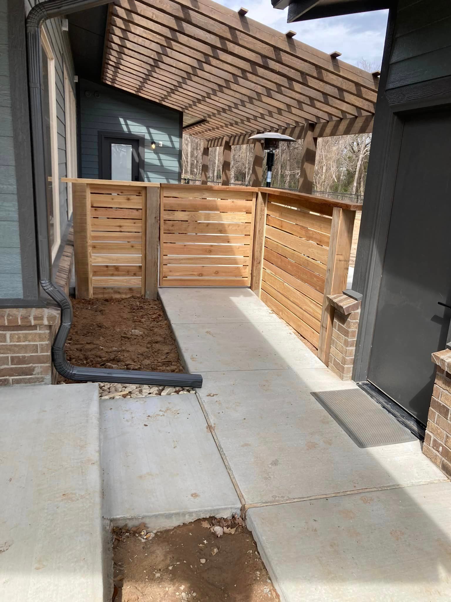 A walkway leading to a house with a wooden fence and a pergola.