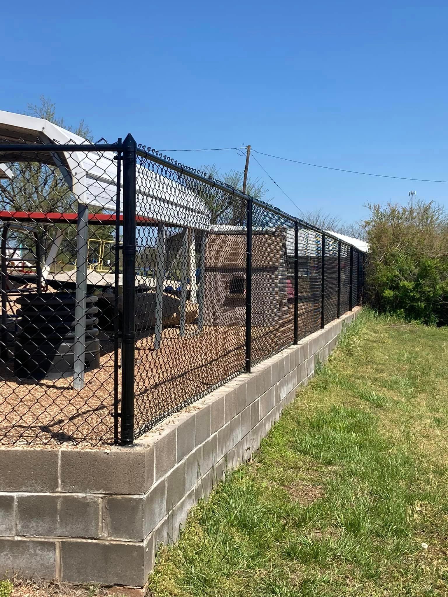 A chain link fence surrounds a brick wall in a yard.