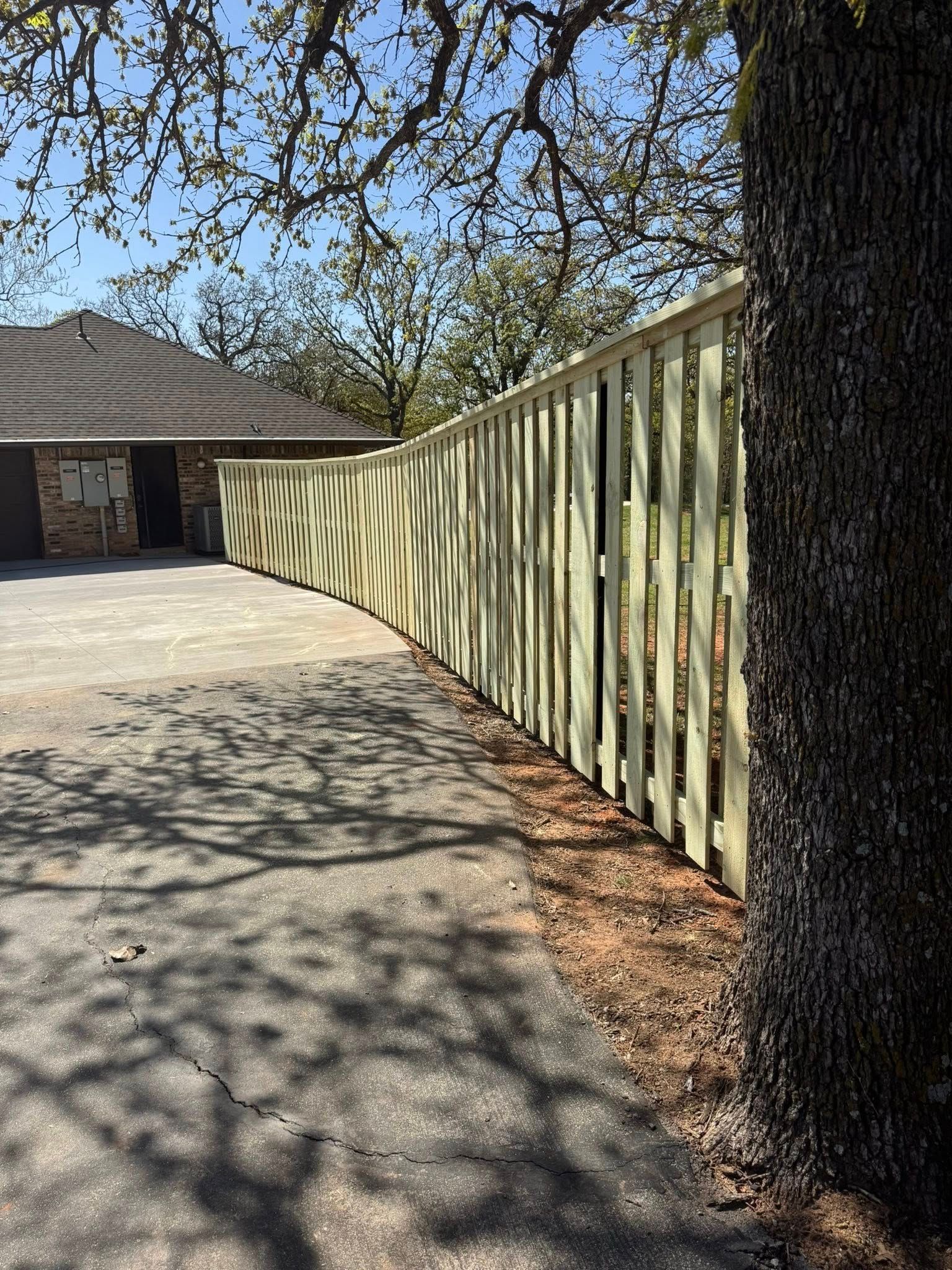 A wooden fence surrounds a driveway in front of a house.