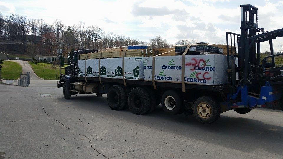 A truck with a forklift attached to it is driving down a road.