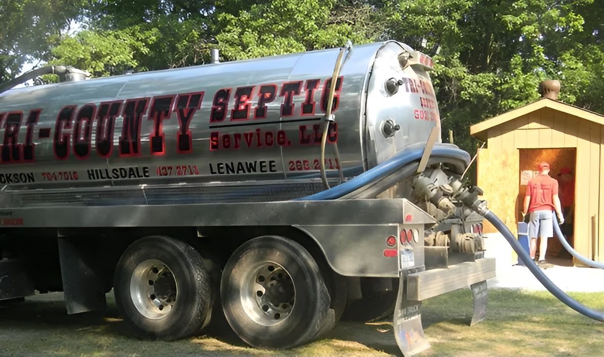 Septic tank truck servicing a small outhouse.