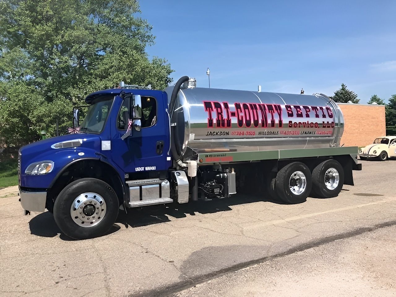 Blue septic tank truck with a silver tank, parked on pavement,