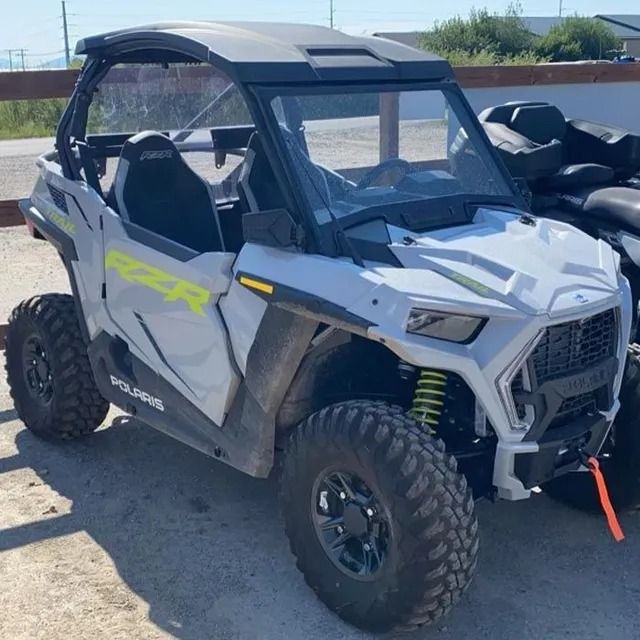 White Polaris RZR side-by-side vehicle with black roof, parked outside.