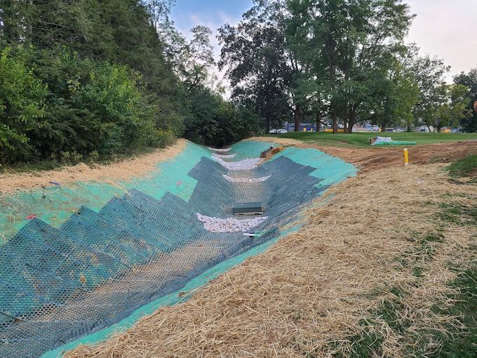 A drainage channel is being built in a park with trees in the background.