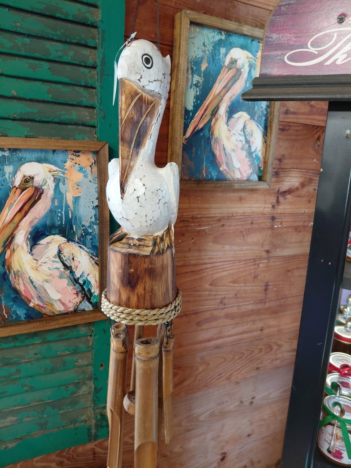 Wooden pelican sculpture beside colorful bird paintings on a rustic wall